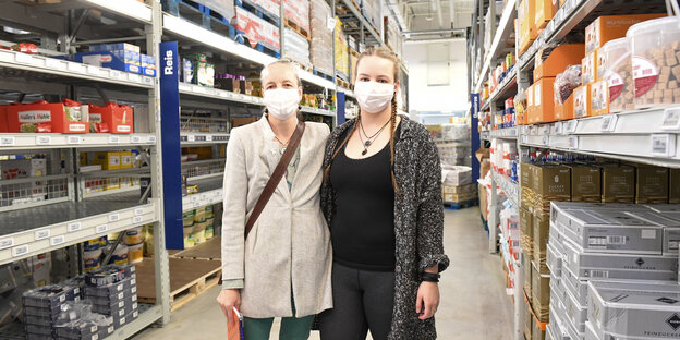 Zwei Frauen mit Mundschutz zwischen Regalen in einem Supermarkt.