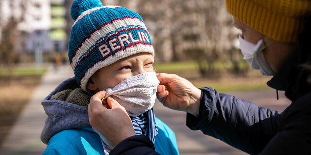 Eine mutter setzt ihrem Kind eine selbstgebastelte Atemschutzmaske auf.