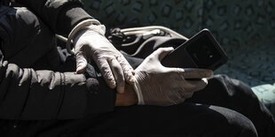 Ein Mensch trägt Schutzhandschuhe und hält ein Smartphone in den Händen