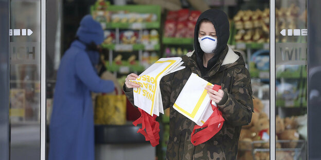 Eine Frau trägt eine Atemschutzmaske und geht durch die Eingangstür eines Supermarkts