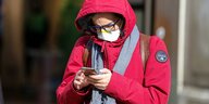 Eine Frau mit Atemschutzmaske schaut auf ihr Smartphone