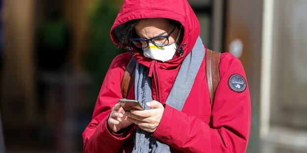Eine Frau mit Atemschutzmaske schaut auf ihr Smartphone