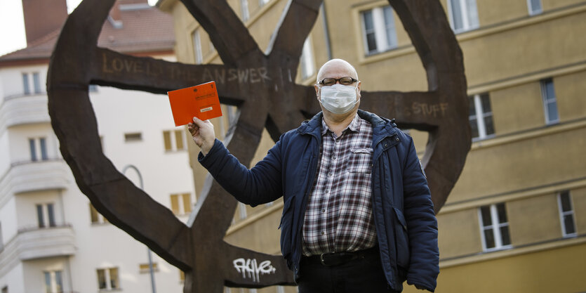 Mann mit Mundschutz hält am Rosa-Luxemburg-Platz ein Grundgesetz in die Luft