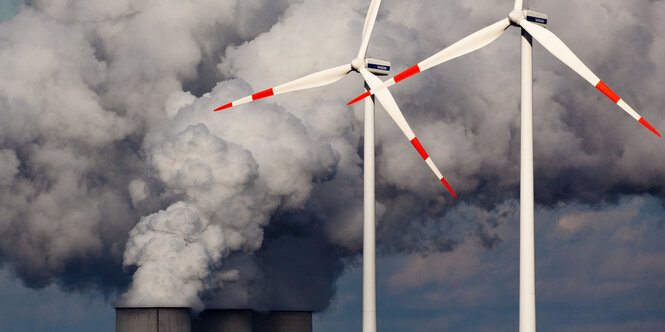 Zwei Windräder vor der Kühlturmen eines Kraftwerks.