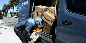 Ein Amazon Fahrer greift Pakete aus der geöffneten Tür eines Lieferwagens.