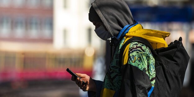 Ein Mann steht an einem Bahnsteig und schaut auf sein Handy