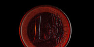 Ein rot angeleuchtete Euromünze vor schwarzem Hintergrund.