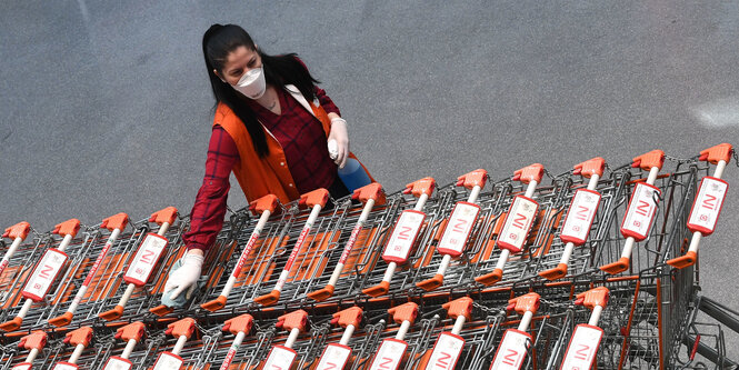 Eine Mitarbeiterin einen Supermarktes mit Mundschutz und Einkaufswagen.