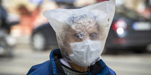 Eine ältere Frau trägt Munschutz und zusätzliche eine Plastiktüte über dem Kopf