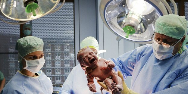 Ärzte in OP-Kitteln halten ein Neugeborenes in die Höhe