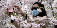 Frau mit Mundschutz zwischen Kirschblüten.