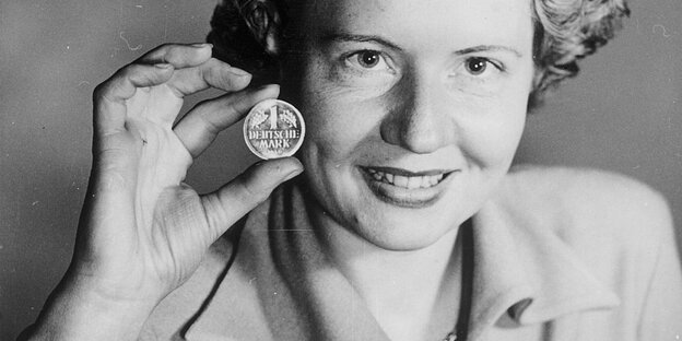 In einem historischen Foto hält eine Frau eine D-Markmünze in die Kamera.