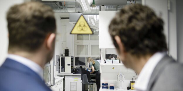 Jens Spahn und Christian Drosten (von hinten fotografiert) gucken gemeinsam in ein Labor