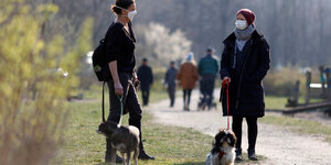 Zwei Menschne stehen mit Masken und ihren Hunden im park