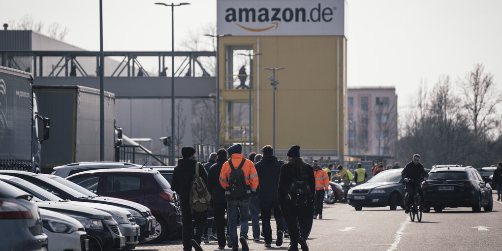 Es laufen viele Mitarbeiter über den Parkplatz beim Amazon-Lager in Leipuig