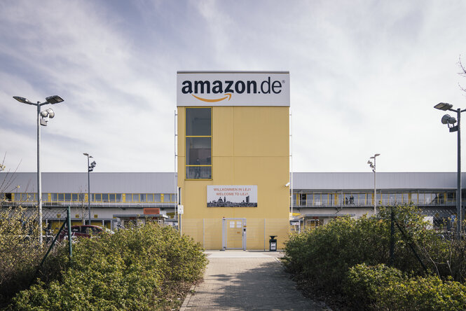 EIngangsbereich zum Amazon Versandzentrum in Leipzig, ein gelbes Gebäude ist zu sehen, auf dem oben der Schriftzug amazon.de steht