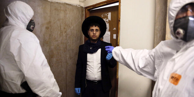 Ein orthodoxer Jude und zwei Polizisten in Schutzkleidung.