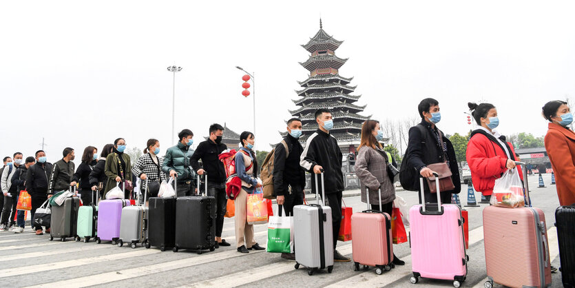 Wanderarbeiter in China stehen mit Gepäck in einer Schlange.