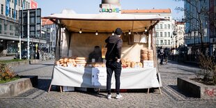 Ein Mann steht vor einem Stand, in dem Brötchen ausgelegt sind.