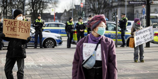 Demonstranten stehen mit Pappschildern und Mundschutz in großem Abstand zueineander auf einem Platz