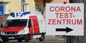 Links ein Krankenwagen, rechts ein Schild Richtung Coronatestzentrum