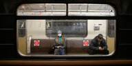 zwei Menschen sitzen inder Ubahn mit Mundschutzmaske