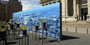 Ein großes Panoromafoto von Hamburg steht vor dem Eingang des Hamburger Landgerichts, davor stehen rostige Kübel mit Blumen