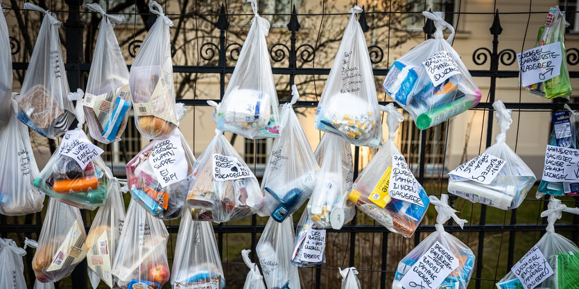 Mit Einkaufswaren gefüllte Plastikbeutel an einem Zaun