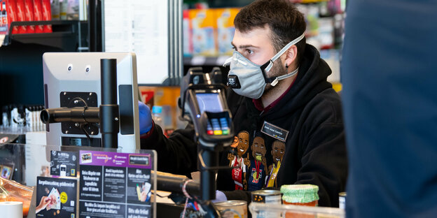 Kassierer im Supermarkt trägt einen Mundschutz