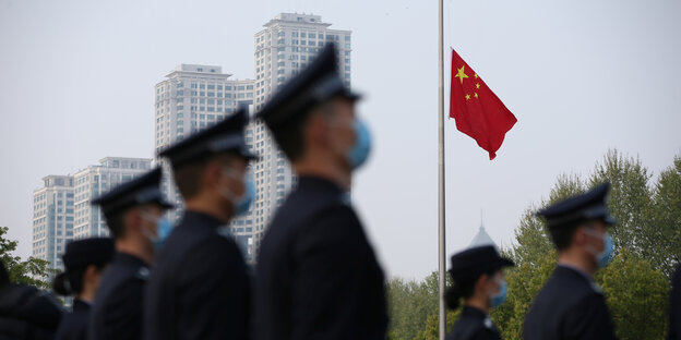 Chinesische Soldaten mit Schutzmasken stehen vor der Nationalflagge auf Halbmast.