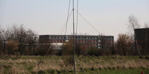 eine Wiese, im Hintergrund erhebt sich ein grau-orangener Plattenbau, der zur Zentralen Anlaufstelle für Asylbewerber in Halberstadt gehört.
