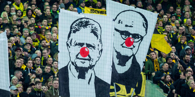 Fans halten Transparente in die Höhe, auf denen der DFB-Chef und Dietmar Hopp Pappnasen auf der Nase haben
