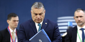 victor Orban mit einer Mappe in der Hand, im Hintergrund zwei Männer