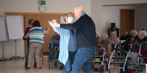 Eine Frau mit Mundschutz tanzt mit einem alten mann