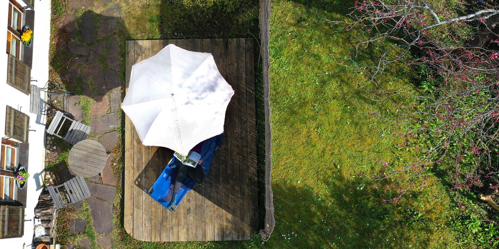 Eine Person liest im Garten unter einem Sonnenschirm