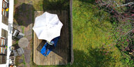 Eine Person liest im Garten unter einem Sonnenschirm