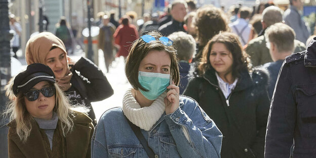 Eine Frau in einer Menschenmenge telefoniert und trägt eine Mundschutzmaske