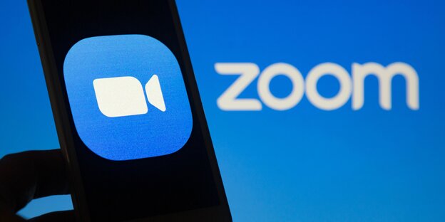 Kamerasymbol weiß auf blau auf einem angeschnittenen Smartphone vor dem Schriftzug "Zoom"