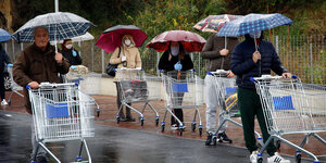 Menschen stehen mit leeren Einkaufswagen in einer warteschlange und haben regenschirme aufgespannt