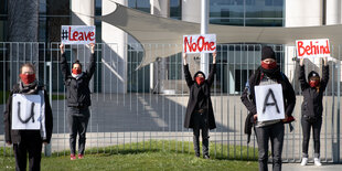 Einzelne Menschen stehen in großen Abständen zueinander und halten Protestplakate hoch