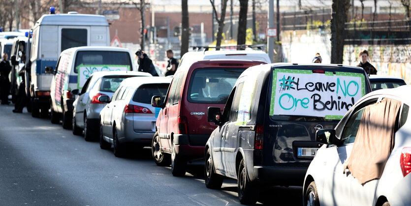 Autos stehen in einer Reihe und sind mit Protestplakaten beklebt