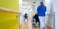 Baden-Württemberg, Böblingen: Eine Pflegerin schiebt eine Bewohnerin eines Pflegeheims in einem Rollstuhl über den Flur.