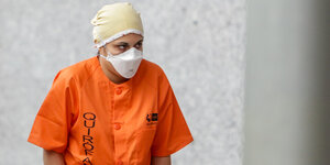 Eine Frau in orangenem Schutzanzug mit Mundschutz lässt die Arme hängen.