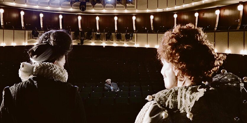 Zwei Schauspieler stehen auf der Bühne eines leeren Theater.