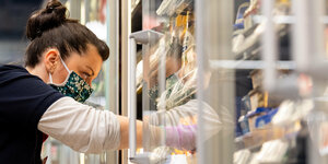Ein Mitarbeiterin in einem Supermarkt bestückt mit Mundschutz ein Rega