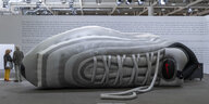 ein riesiger grauer aufgeblasener Turnschuh der Marke Nike liegt als Skulptur in der Messehalle der Art Basel 2019