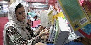 Eine Frau mit Kopftuch sieht sich ein Buch auf einer Messe an.