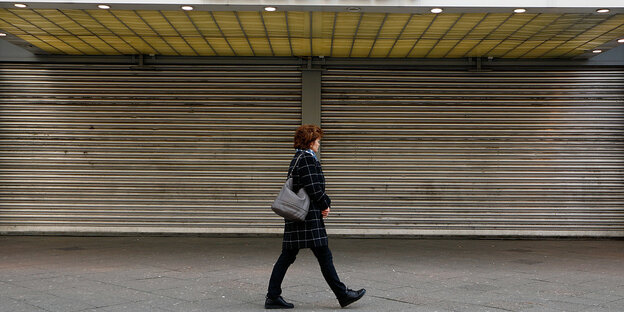 Eine Frau lüft an geschlossenen Schaufensterläden einer Karstadt-Filiale entlang