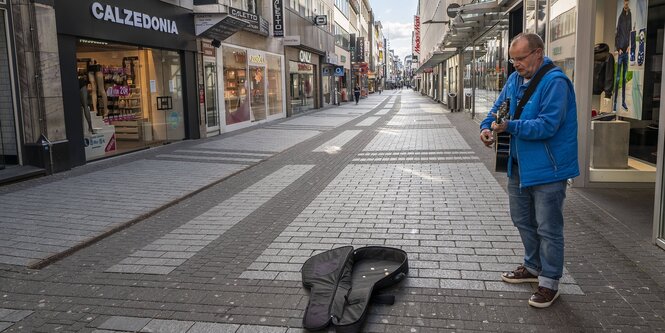 Ein Strassenmusiker steht allein in einer Fussgängerzone