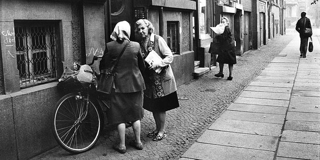Eine Briefträgerin spricht mit einer Frau, die ein Kopftuch trägt
